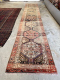 Narrow Persian runner featuring tribal medallions and abrash wool variation.