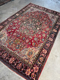 Antique Ferahan Persian rug with a berry red ground and central medallion, lying flat on a grey concrete floor.