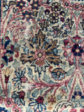 Muted floral antique Persian rug on a neutral sand background with blue accents.