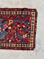 One end of Persian rug with garnet red field and tribal motifs.