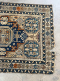 Worn low pile Caucasian rug in neutrals, blues, and warm orange accents.