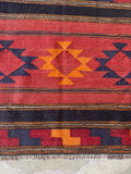 Close up of antique tribal flatweave textile with graphic bands of red, navy, and saffron vegetable-dyed wool.