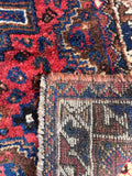 Small hand-knotted Persian area rug with vibrant berry red, deep blue, and warm brown dyes.