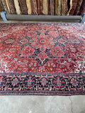 Large Persian Heriz carpet. Antique tribal rug with architectural design, vivid reds, deep navy, and exceptional durability for everyday living.