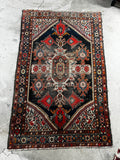 Hand-knotted tribal wool rug with low pile, scattered wear, and detailed paisley vine artwork.