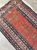 Turn of the 20th century Persian area rug in 5' x 9' size with heavy antique distressing and low pile.