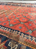 Distressed antique Persian lattice rug flat-lay detail showing low wool pile and rich terracotta tones.