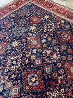 Diagonal view of Persian Heriz rug showcasing moody navy field and berry red borders.