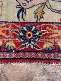 Handwoven pictorial rug close-up shot of the contrast between the pale green field and red floral frame.