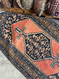Coral field Malayer rug with navy medallion full of small tribal motifs.