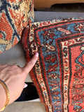 Close up photo of finger pointing to a tiny mended repair on an antique rug border.