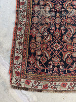 Corner view of antique Persian rug with small paisley border details.