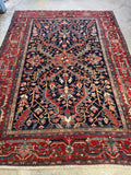View of an early 1900s Heriz rug featuring a deep moody navy field and wide rust red borders.