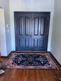 A dark navy blue entryway rug with a traditional floral pattern, placed on a hardwood floor in front of a dark navy double door.