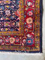 Corner view of vintage Persian scatter rug featuring a navy field and red border.