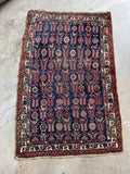 Worn navy Persian wool rug with a low pile and colorful geometric design.