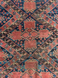 Close view of antique Persian rug displaying low pile wool and geometric tribal motifs.
