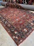 Antique Persian Heriz rug from early 1900s with terracotta red field and botanical motifs.