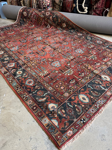 Antique Persian Heriz rug from early 1900s with terracotta red field and botanical motifs.