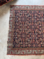 One end view of Low pile Persian rug with floppy handle and worn areas.
