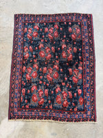 Full view of an antique Persian Bidjar rug with red floral patterns on a dark blue background.
