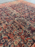Handwoven Persian rug featuring navy field and rust borders.