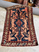 Full view of Persian rug with bold tribal design and abrash pink ground.