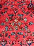 Detail view of hand knotted antique Persian rug showing floral motifs against a coral ground.