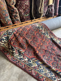 Antique red Persian Kurdish runner rug 4x12 draped in rug shop showing full pattern