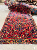 Small red Persian scatter rug with indigo, camel and green floral motifs.