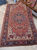 Antique Persian Heriz rug 5x9 top-down view displaying a cantaloupe field, sharp geometric medallion, and rich navy borders.