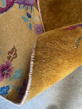 Underside view of small antique Chinese rug with an open field and decorative landscape scene.