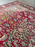 Hand-knotted antique wool rug displaying natural abrash color shifts across a rich berry and navy blue field.