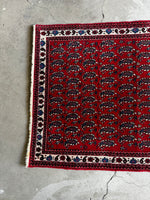 Compact vintage Persian rug with rows of paisley patterns and ivory accents.