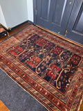 A traditional oriental area rug with a dark navy blue field, red floral motifs, and beige borders, shown on a wooden floor in front of dark gray double doors.