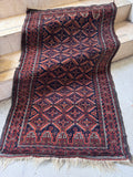 Antique Baluchi tribal rug 3x4 laid flat on concrete, featuring a deep navy blue and crimson red geometric lattice pattern.