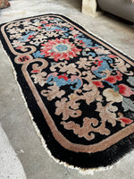 Close-up of coral swastika symbol on Chinese rug, framed by florals and cloudband scrolls

