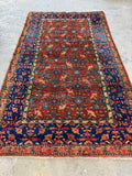 Full view of Persian rug with a terracotta wool ground with floral motifs.