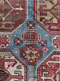Close up of antique tribal rug from the Caucasus with hexagonal medallions and symbolic motifs.