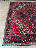 Antique Persian Heriz rug. Oversized hand knotted wool carpet with a bold brick red field, floral chain border, and minimal wear.