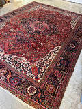 Antique Persian Heriz rug with a deep crimson field and coral medallion, sized 10' x 13'.