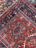 Antique Persian Heriz rug angled garden view, rust red field and navy border
