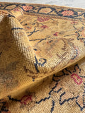 Close-up detail of vintage Turkish rug field showing scrolling floral vine in camel, gold and dusty rose on warm ground