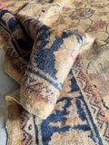 Close-up corner detail of vintage Turkish rug field showing scrolling floral vine in camel, gold and dusty rose on warm ground