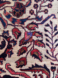 Close up view of botanical design against an ivory ground for an antique Persian rug, also showing small, discreet vintage patch.