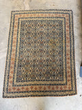Antique Persian rug with Herati pattern laying flat on concrete floor, showing full view of blue and tan wool design.