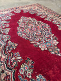 Vegetable dyed red Persian area rug close up showing luminous wool pile and intricate navy and ivory floral details.