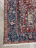 Tribal Persian area rug corner closeup highlighting intricate navy blue border artwork.