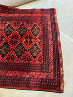 One end view of rug with red and navy pattern highlighting tribal artistry of Afghan weaving.