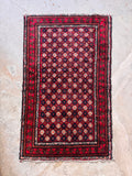 Vibrant red Persian Baluchi scatter rug top-down view highlighting rich crimson tones, navy accents, and complex tribal borders.